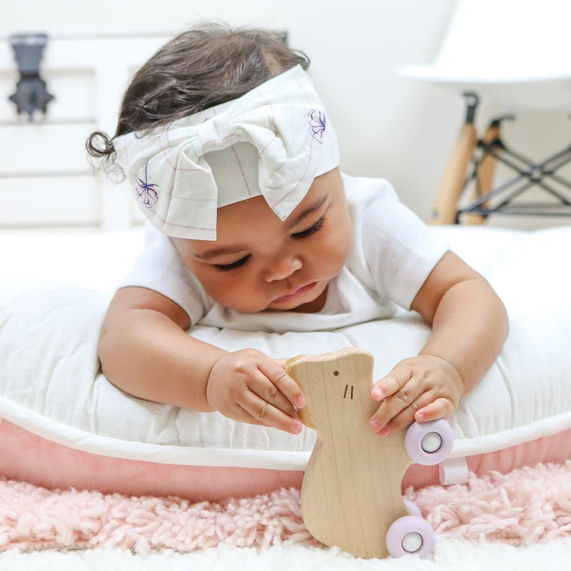 A baby playing with the Silicone + Wood Teether with Wheels, exploring its charming wooden design and smooth rolling wheels, perfect for babies aged 4 months and up.