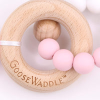 Wooden ring teether with pink silicone beads and a white ribbon.