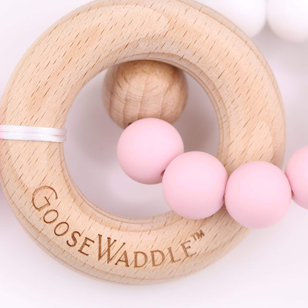Wooden ring teether with pink silicone beads and a white ribbon.