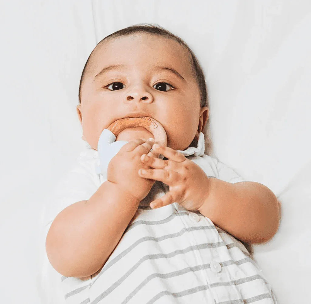 Baby holding and chewing on a blue and natural wood wooden silicone baby teether while lying down