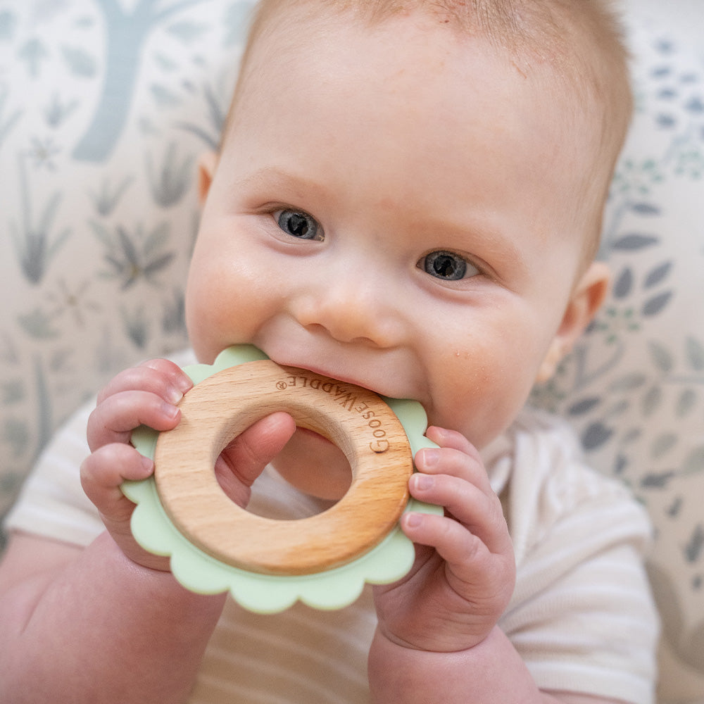 Baby chewing on pastel green and natural wooden teether ring from Goosewaddle for newborns