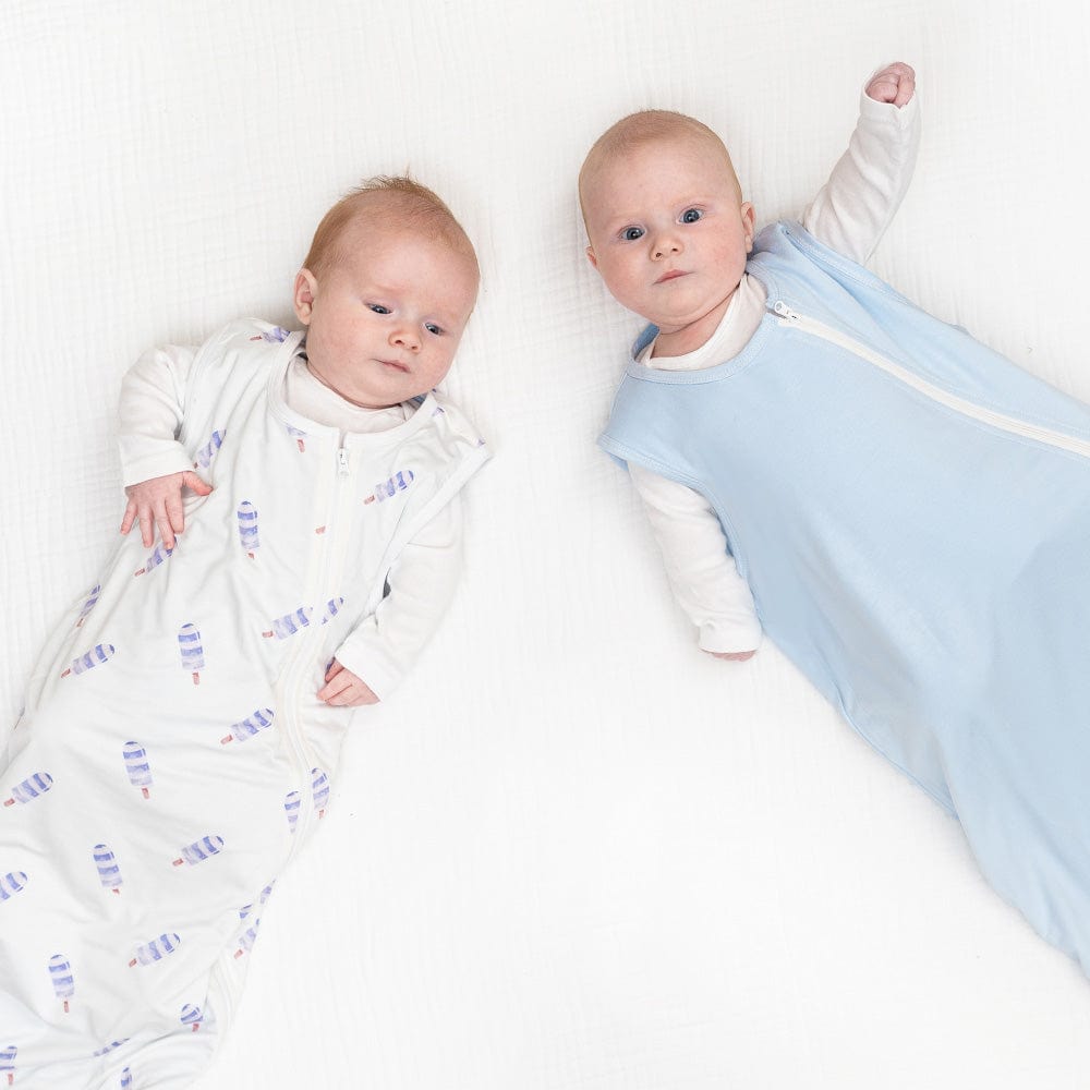 Two infants in Goosewaddle® Zippered Sleep Sacks on a soft, white surface, showcasing comfort and style for peaceful sleep.
