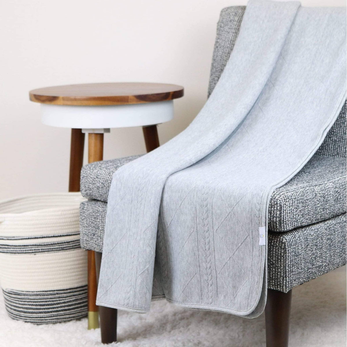 Gray knit baby blanket made of soft material draped over a gray chair in a cozy room setting