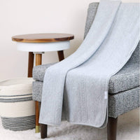 Gray knit baby blanket made of soft material draped over a gray chair in a cozy room setting