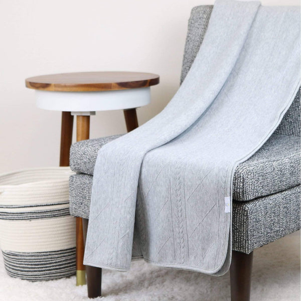 Gray knit baby blanket made of soft material draped over a gray chair in a cozy room setting