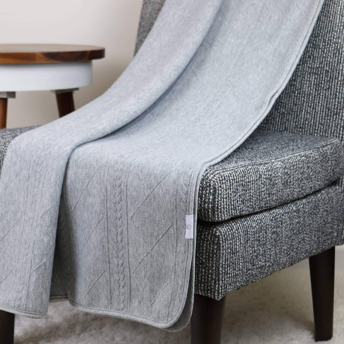 Gray knit baby blanket made of soft material draped over a gray textured chair