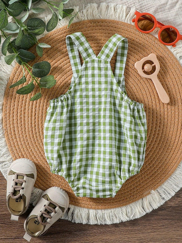 Green checkered baby romper laid flat with baby shoes and toy on round woven mat