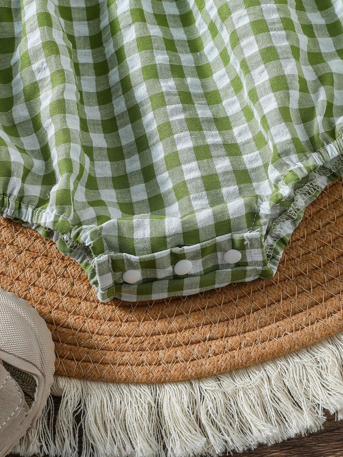 close-up of green checkered baby romper with snap buttons on a woven mat background
