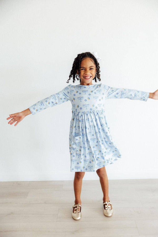 girl wearing light blue Hanukkah dress for girls with long sleeves smiling and spreading arms