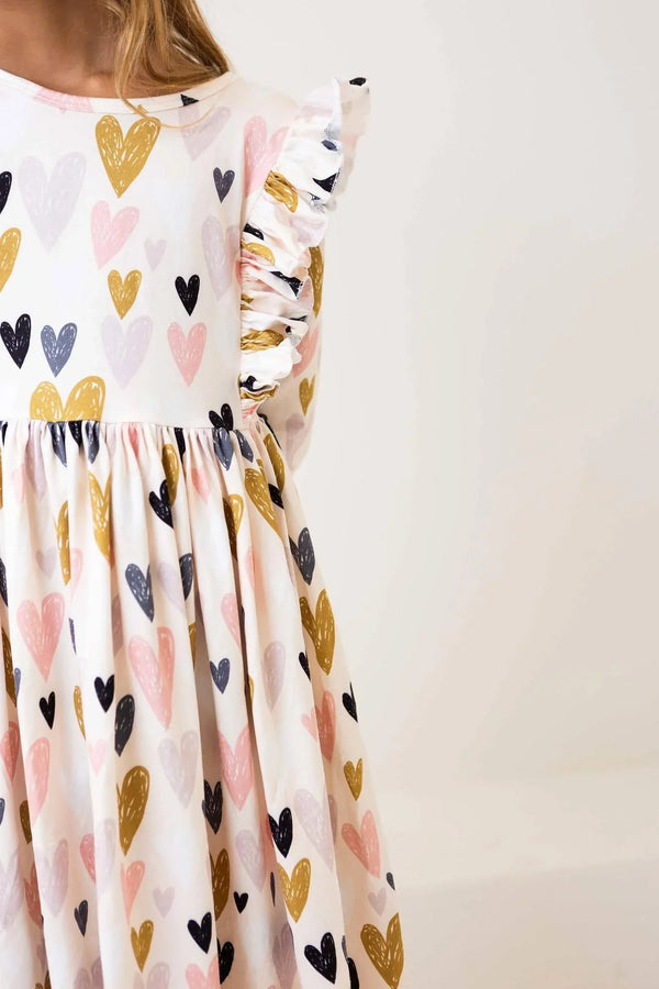 young girl wearing white heart print ruffle twirl dress with pink gold and black hearts