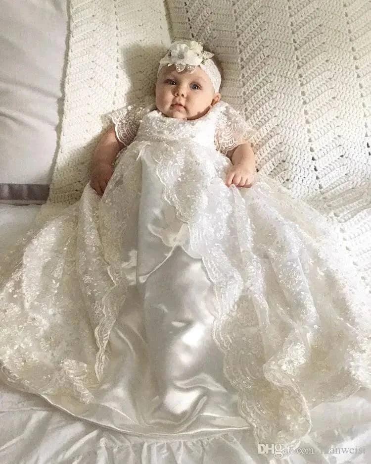 baby wearing white heirloom christening gown for babies with lace and satin details lying on a crocheted blanket
