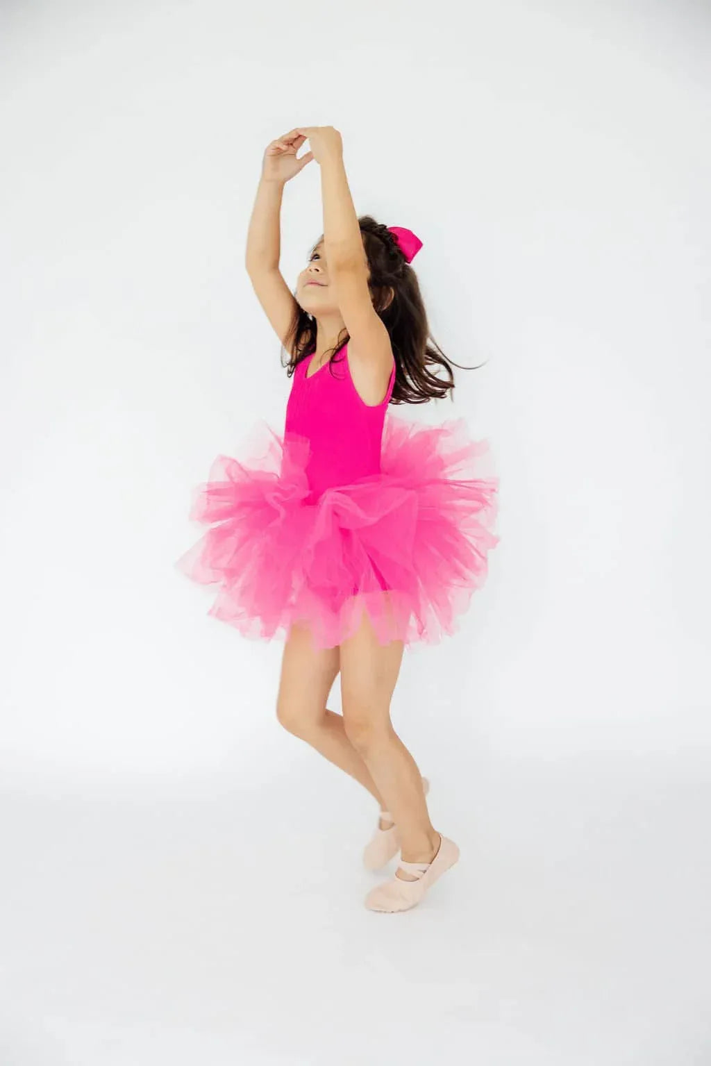 young girl wearing hot pink tutu leotard dancing with arms raised and light pink ballet shoes