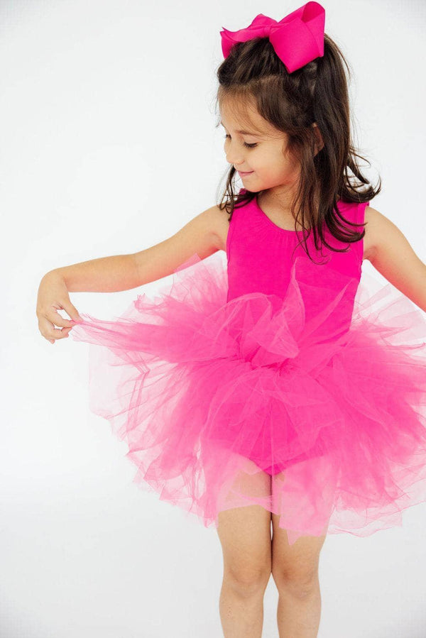 young girl wearing hot pink tutu leotard holding ballet skirt and smiling