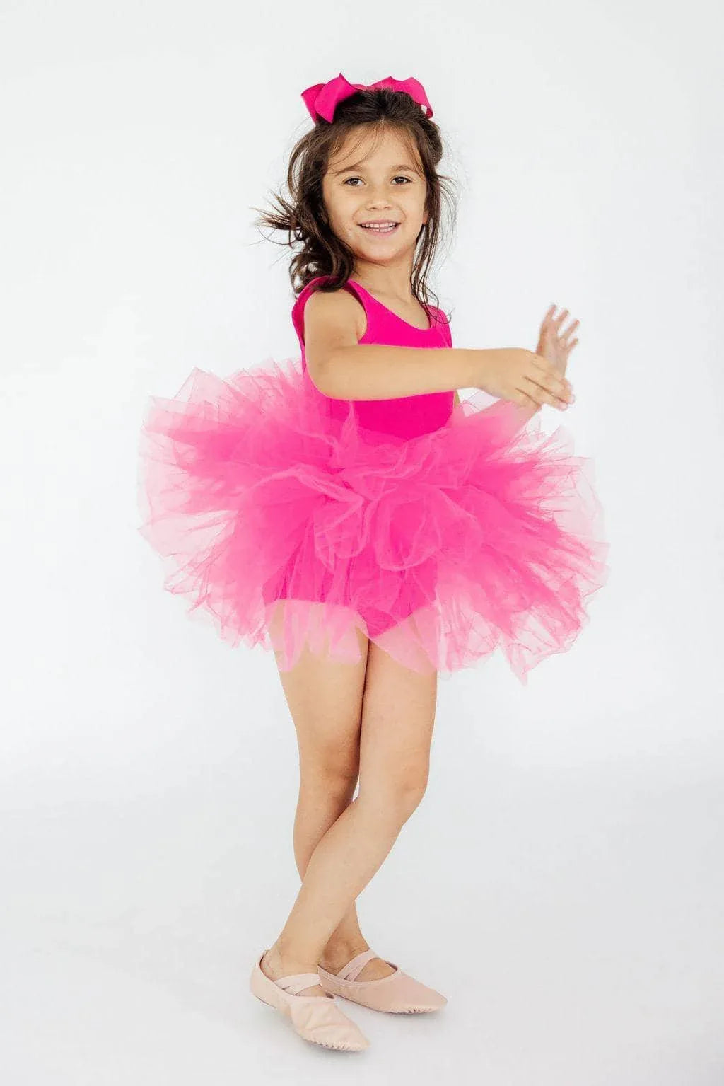 young girl wearing hot pink tutu leotard smiling and posing with arms extended