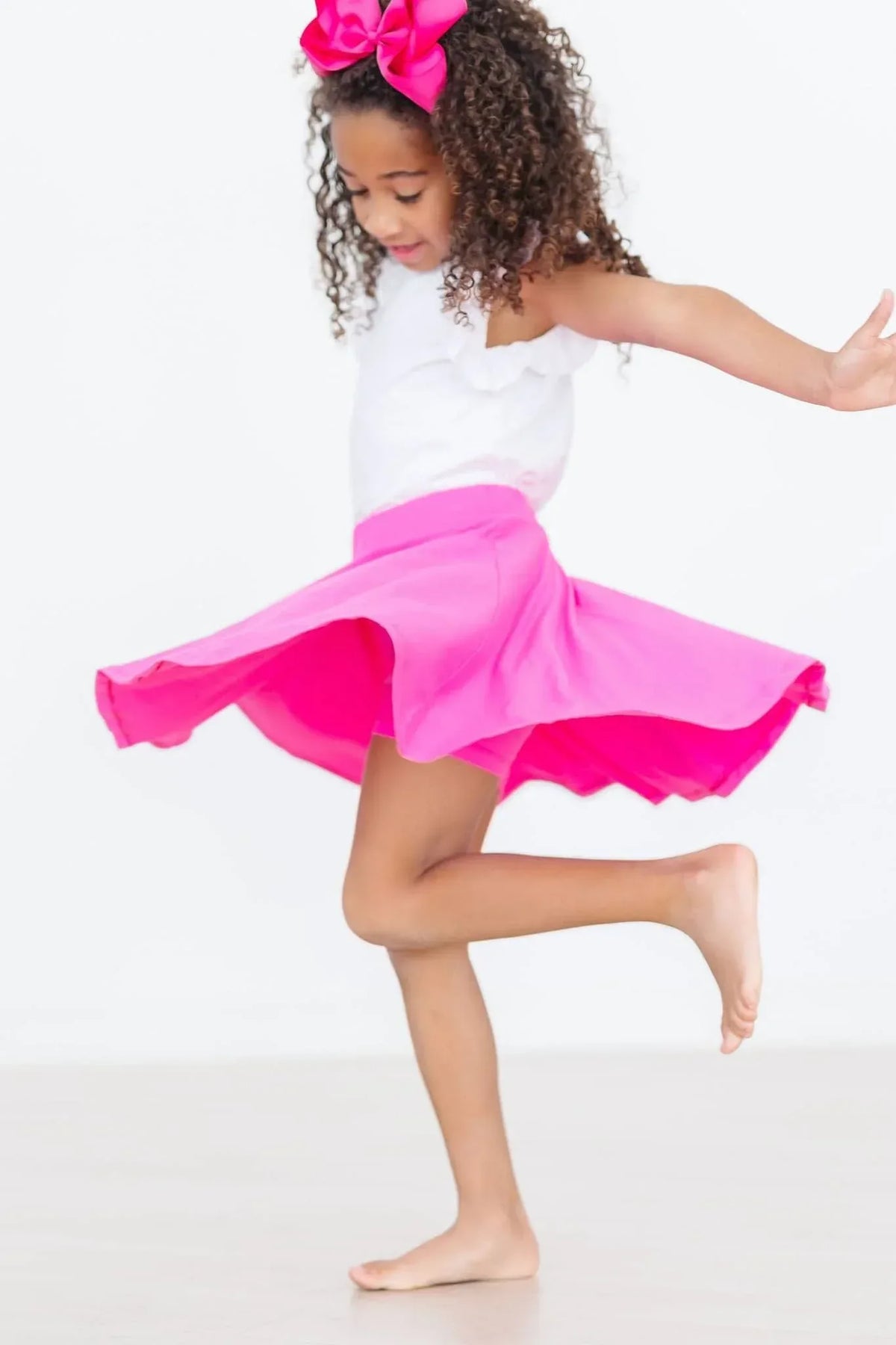 little girl wearing hot pink twirl skort for girls spinning barefoot with a matching pink bow
