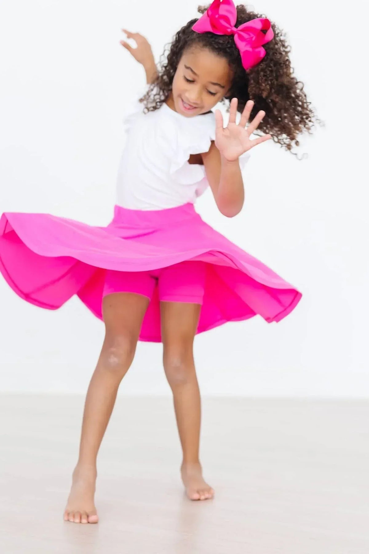 Girl wearing hot pink twirl skort for girls spinning with arms raised indoors