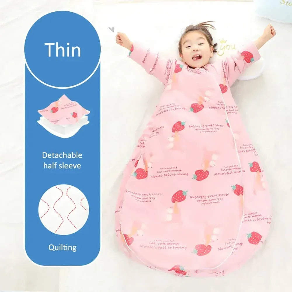 Toddler girl wearing pink zippered sleeping bag for kids with strawberry print lying on white surface with arms raised