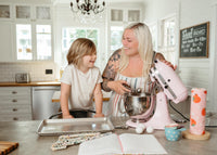 Woman and child in a kitchen using a pink stand mixer.