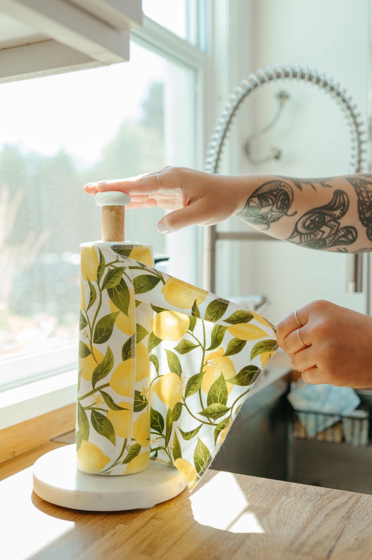 Person holding a lemon-patterned kitchen towel over a bottle with a window in the background