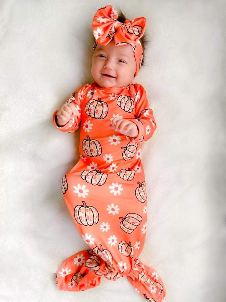 A smiling baby wearing the Cute Leopard Pumpkin Outfit, featuring a vibrant orange swaddle gown with playful leopard and pumpkin designs, paired with a matching headband. Perfect for fall celebrations!