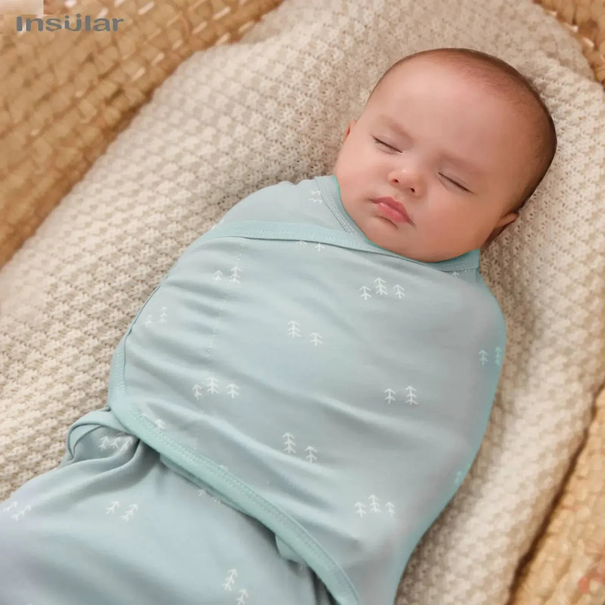 Light blue cotton swaddle bags for babies with white tree pattern wrapped around sleeping infant