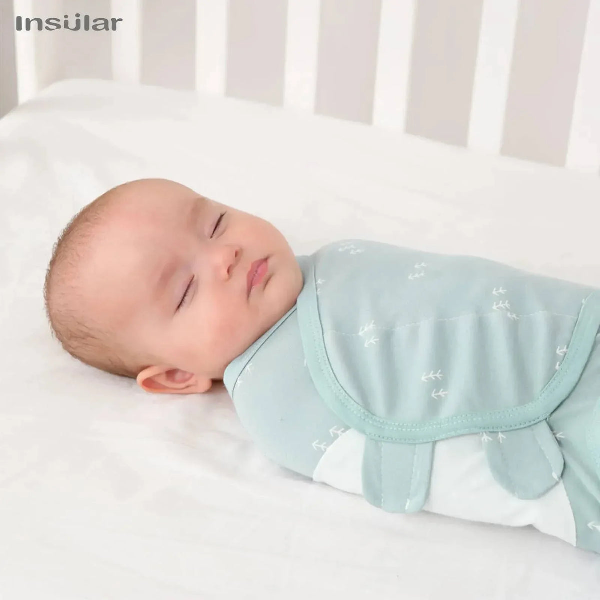 Light blue cotton swaddle bags for babies with white leaf patterns wrapped around a sleeping baby