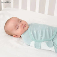 Light blue cotton swaddle bags for babies with white leaf patterns wrapped around a sleeping baby