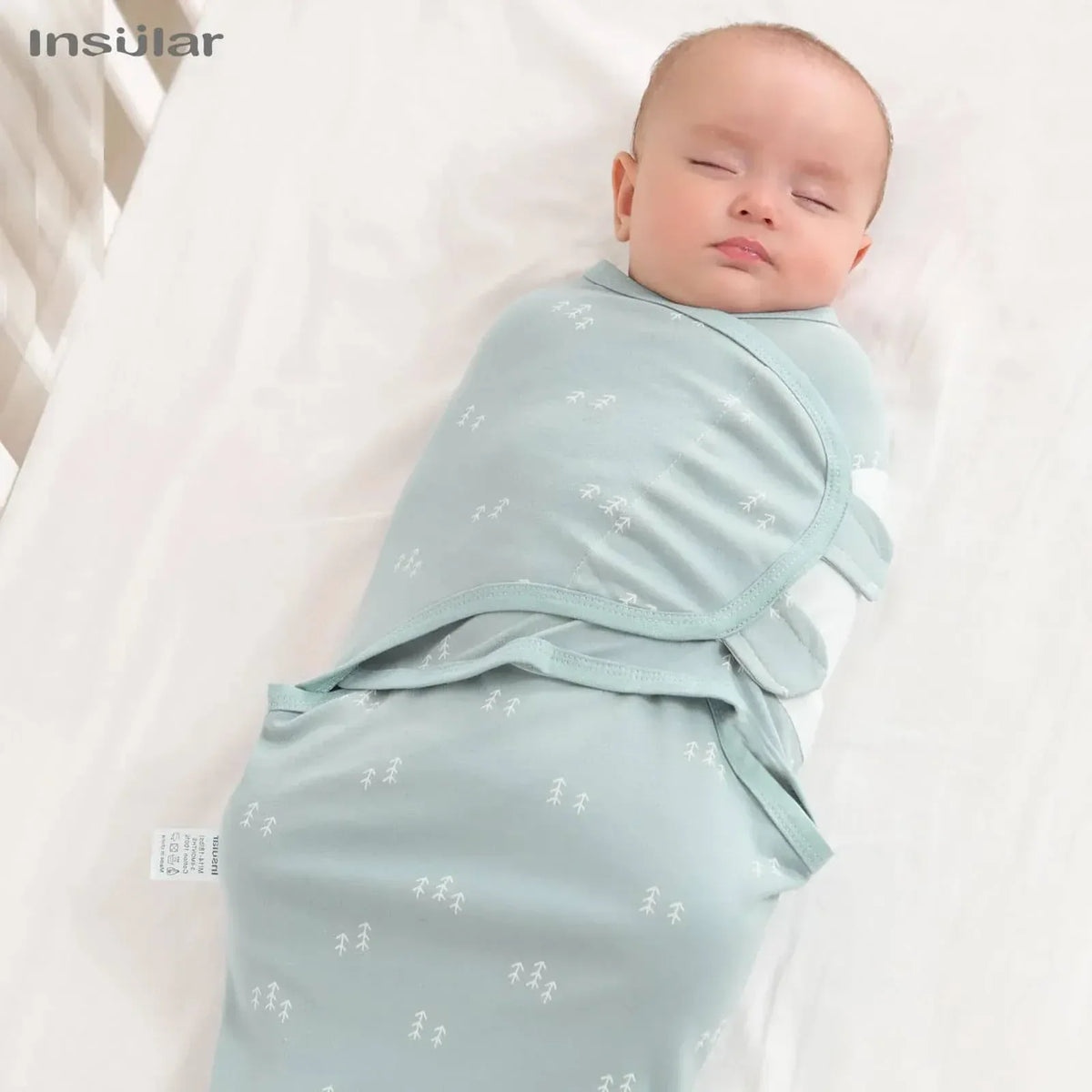Light blue cotton swaddle bags for babies with small white prints wrapped around sleeping infant
