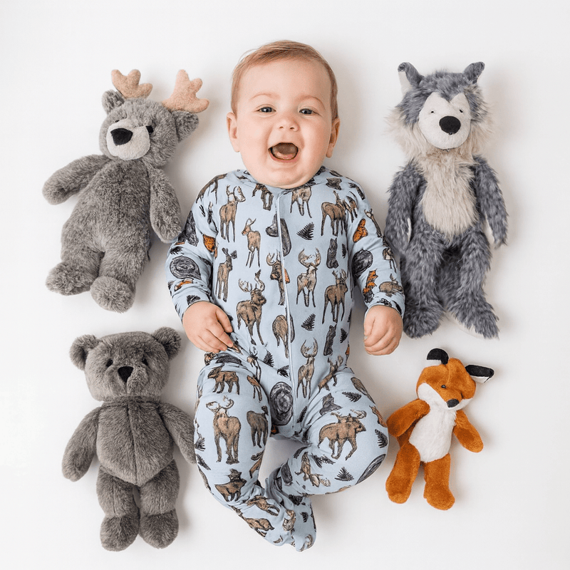 Baby in a onesie with animal patterns surrounded by stuffed animals on a white background