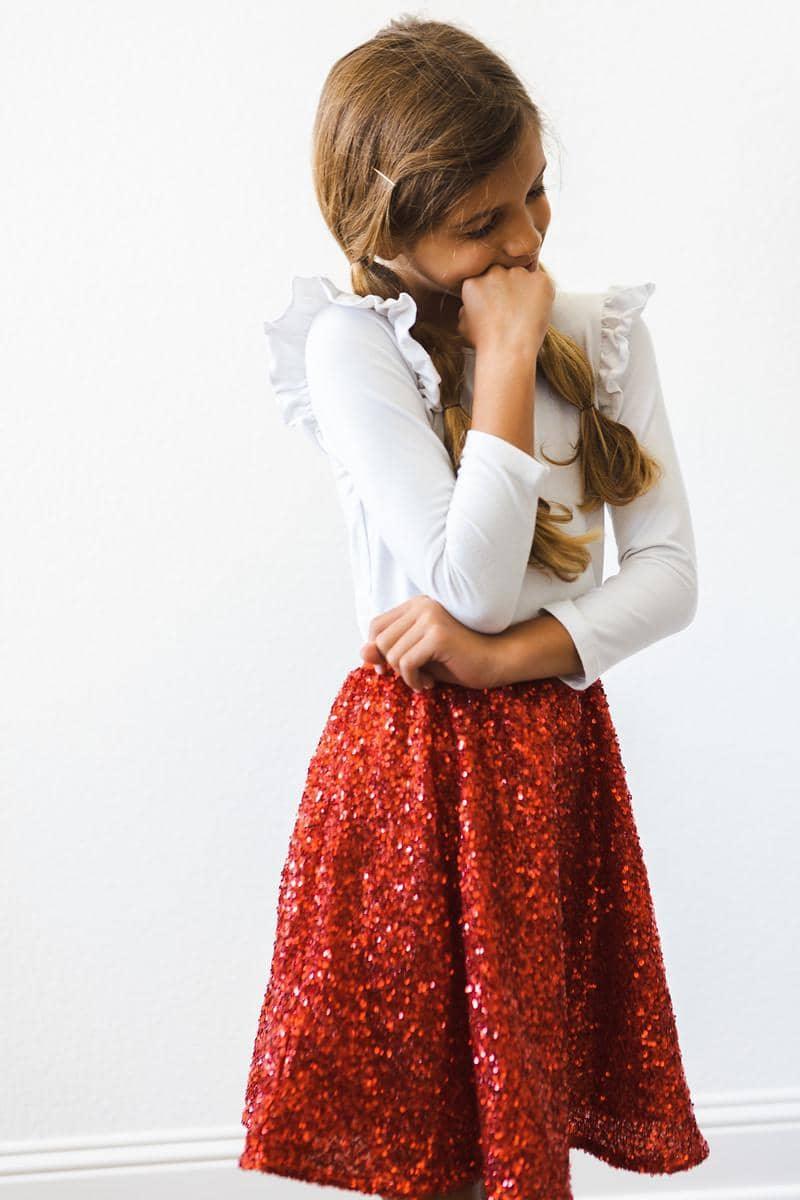 Girl wearing kids red sequin skort standing and looking down with hand near mouth