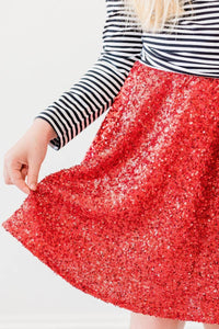 Girl wearing kids red sequin skort holding the hem of the skirt with striped long sleeve top