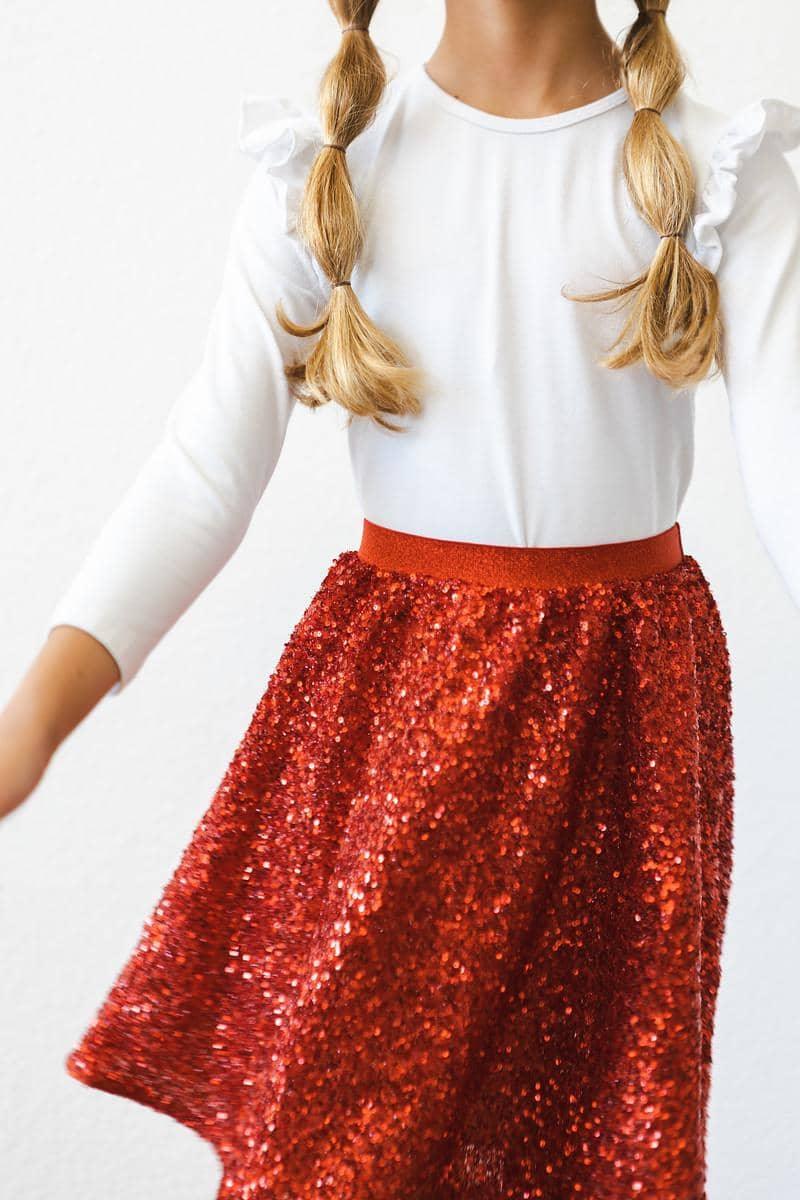 Girl wearing kids red sequin skort twirling with white long sleeve ruffle top