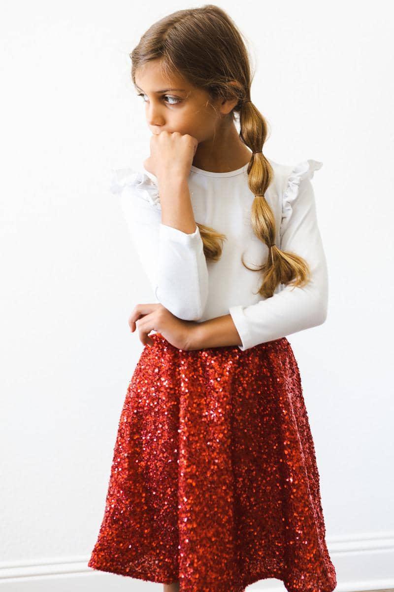 girl wearing kids red sequin skort standing with hand near face looking thoughtful