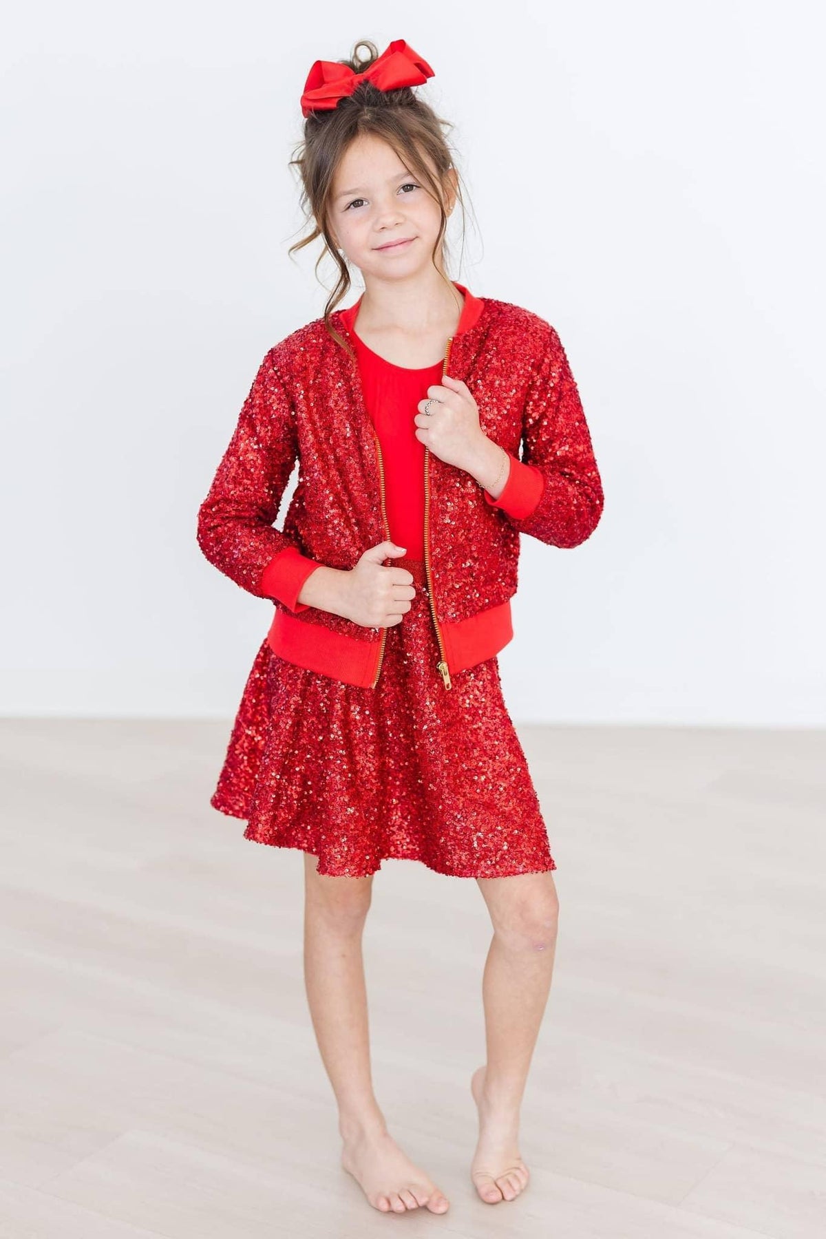young girl wearing kids red sequin skort with matching sequin jacket and red bow standing barefoot