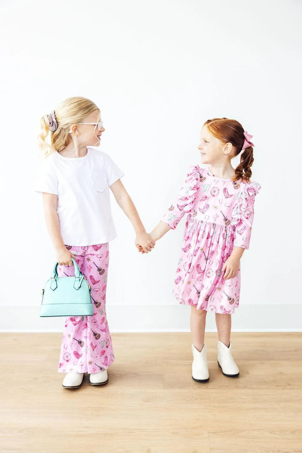 Girls pink kids ribbed velvet bell bottoms with heart pattern, worn by child holding hands with girl in pink dress