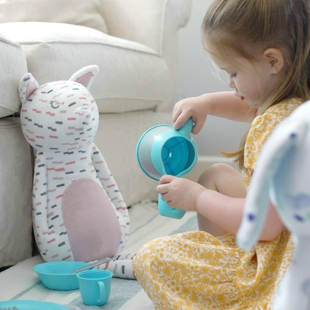 Printed white and pink kitty plush toy with colorful dashes sitting next to toddler in yellow dress