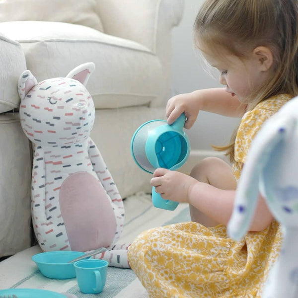 Printed white and pink kitty plush toy with colorful dashes sitting next to toddler in yellow dress
