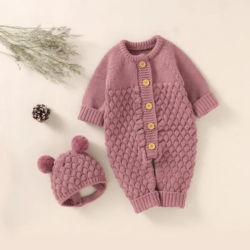 Baby pink knit romper set with textured pattern and wooden buttons for newborns including matching hat with pom poms