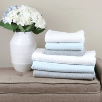 Full size knit throw blankets in white, light blue, and gray stacked next to white vase with flowers