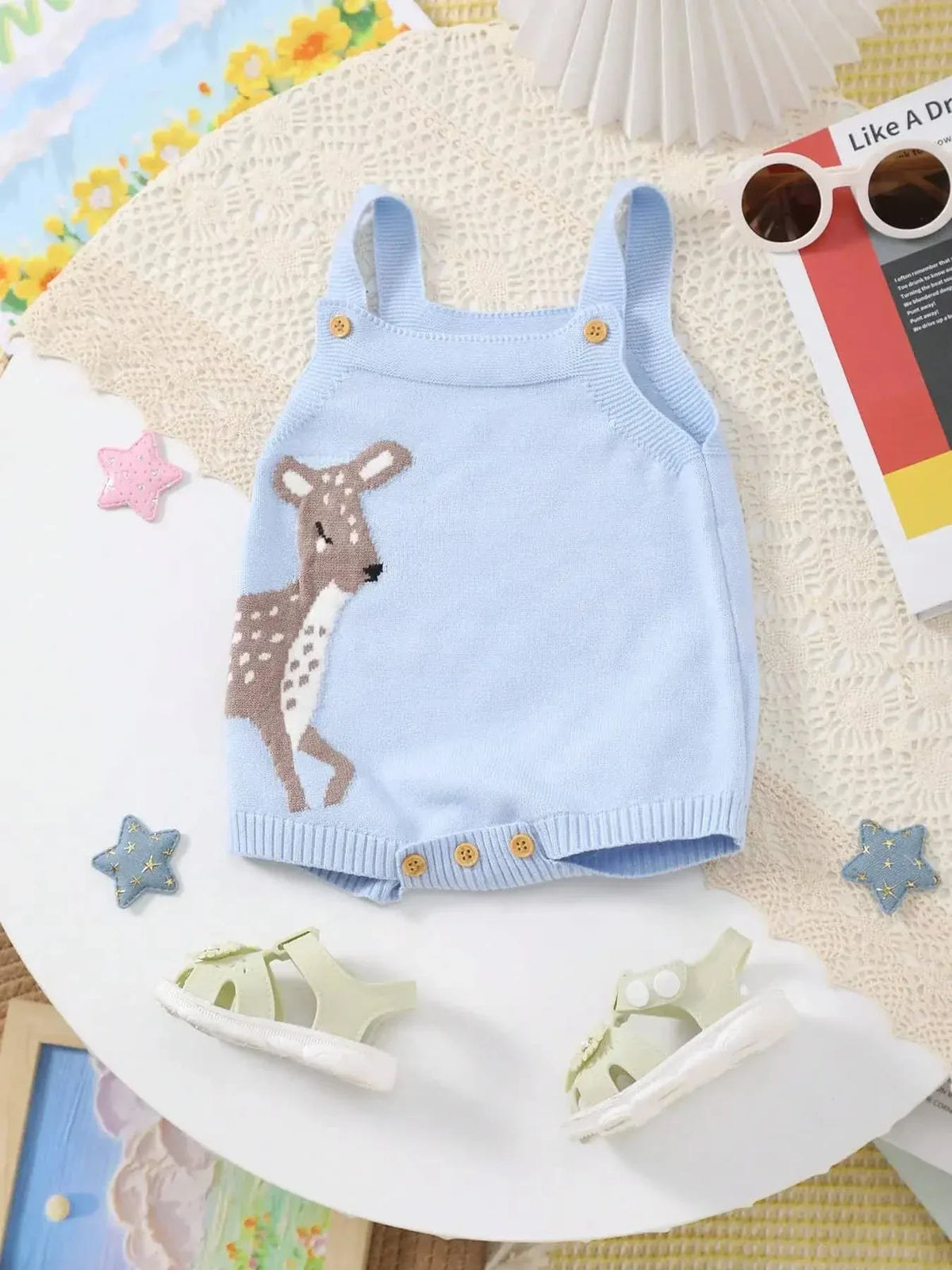 Light blue knitted baby bubble romper with deer design for infants laid flat with white sandals