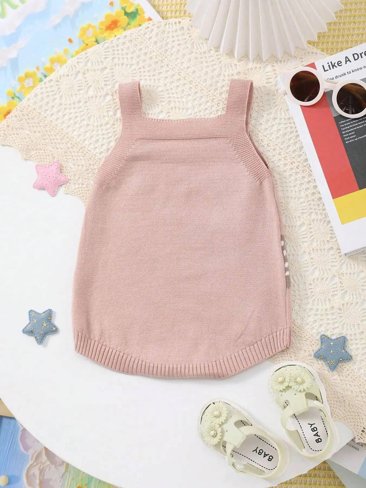 pink knitted baby bubble romper for infants laid flat on white lace background with baby shoes