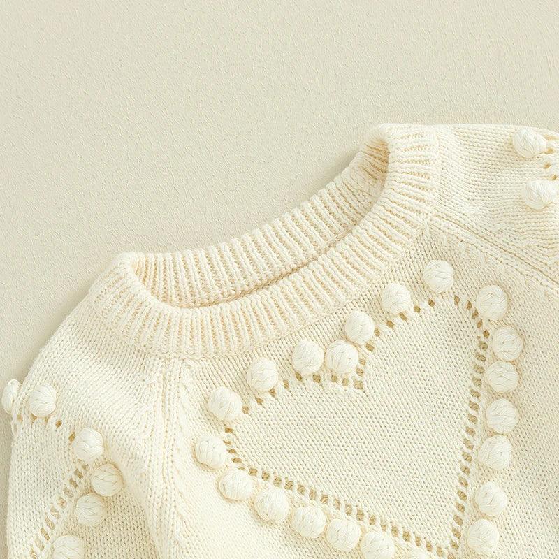 cream knitted baby romper for newborns with heart pattern and pom pom detailing