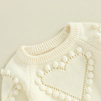 cream knitted baby romper for newborns with heart pattern and pom pom detailing