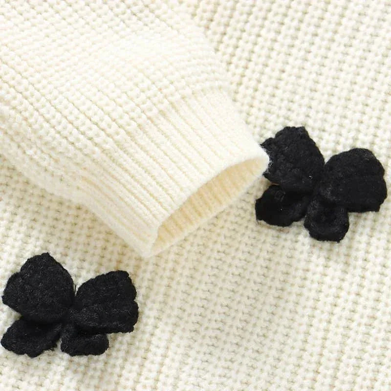 close-up of cream knitted baby romper with bows showing sleeve and black bow details