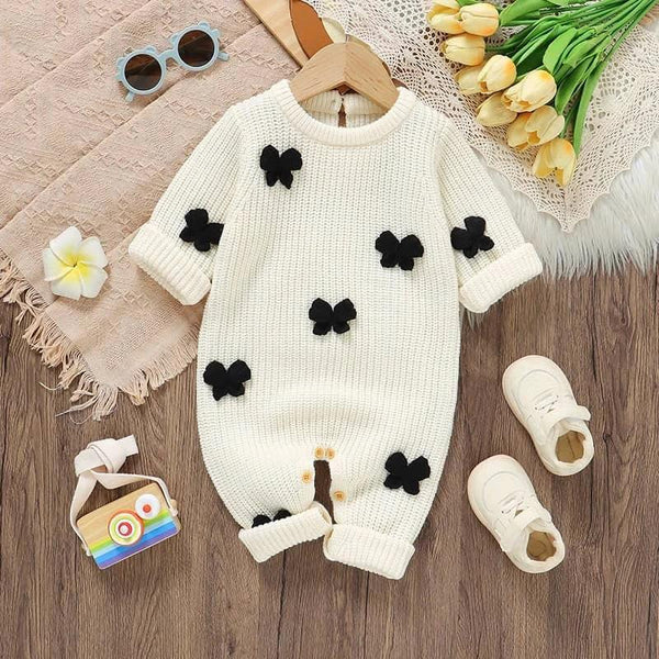 Cream knitted baby romper with bows for infants displayed with white shoes and sunglasses