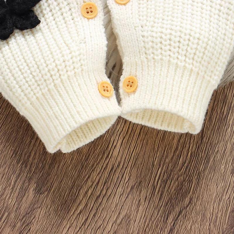 close-up of cream knitted baby romper with bows showing button details for infants