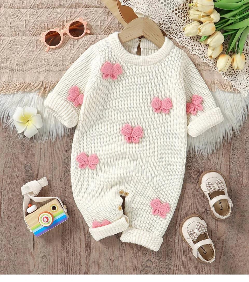 white knitted baby romper with bows in pink for infants displayed with baby shoes and sunglasses