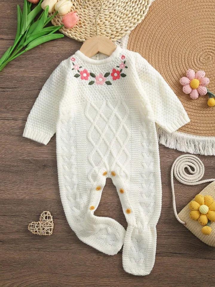 white knitted baby romper with feet sized for infants featuring floral embroidery on chest displayed on wooden hanger
