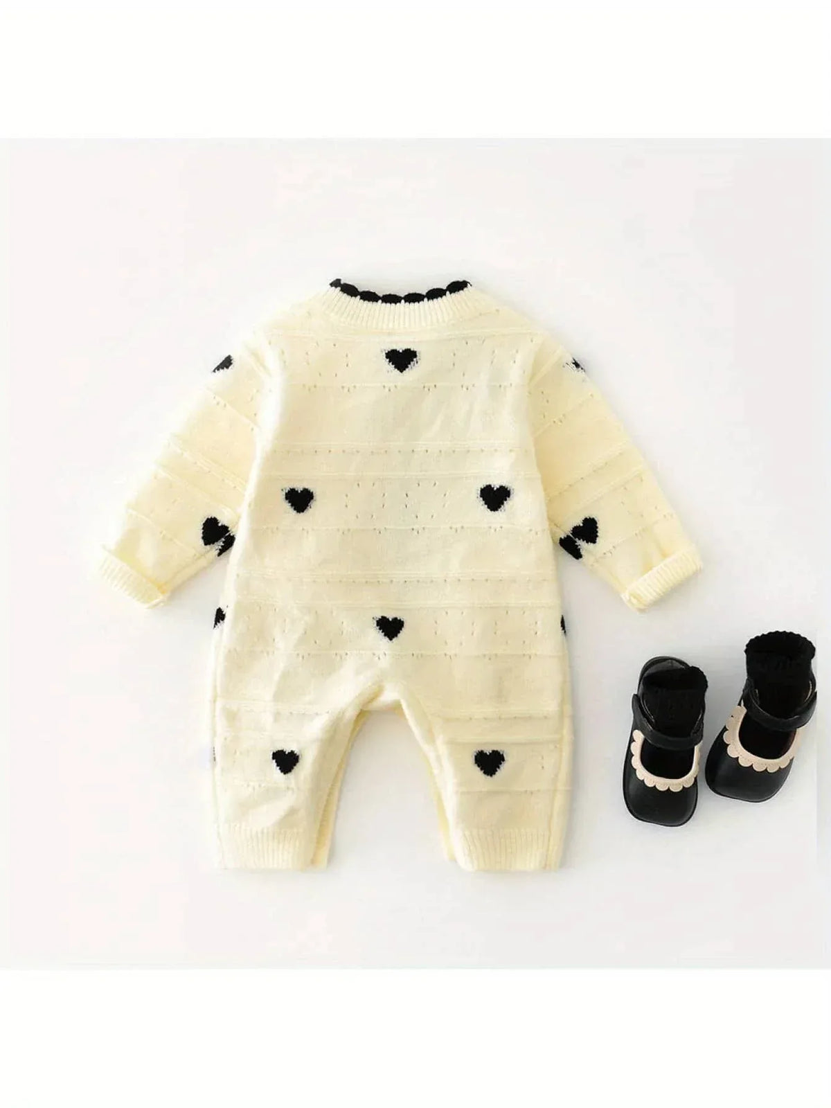 Cream knitted baby romper with hearts in black for infants laid flat with black baby booties