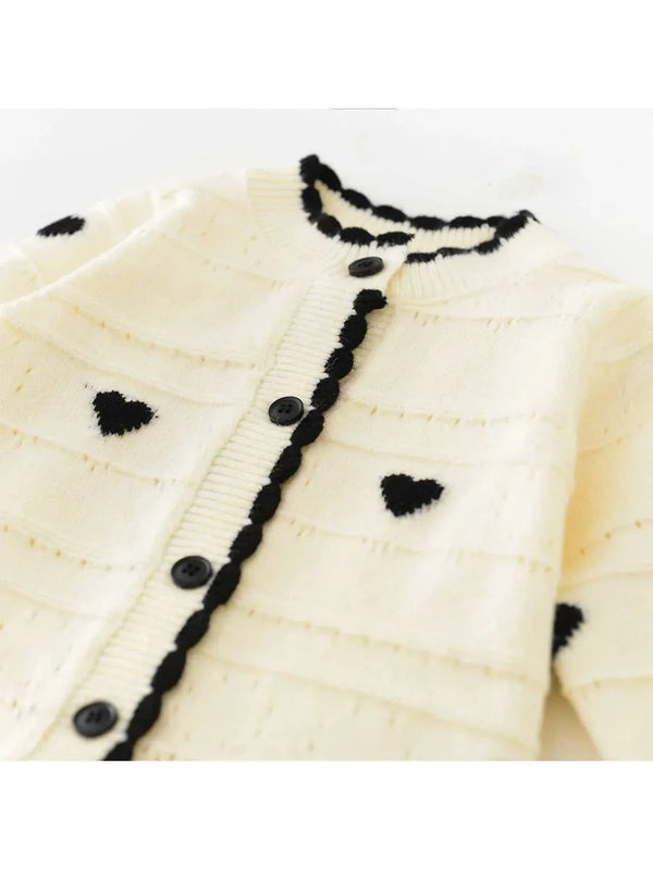 Cream knitted baby romper with hearts in black for infants, laid flat showing button details